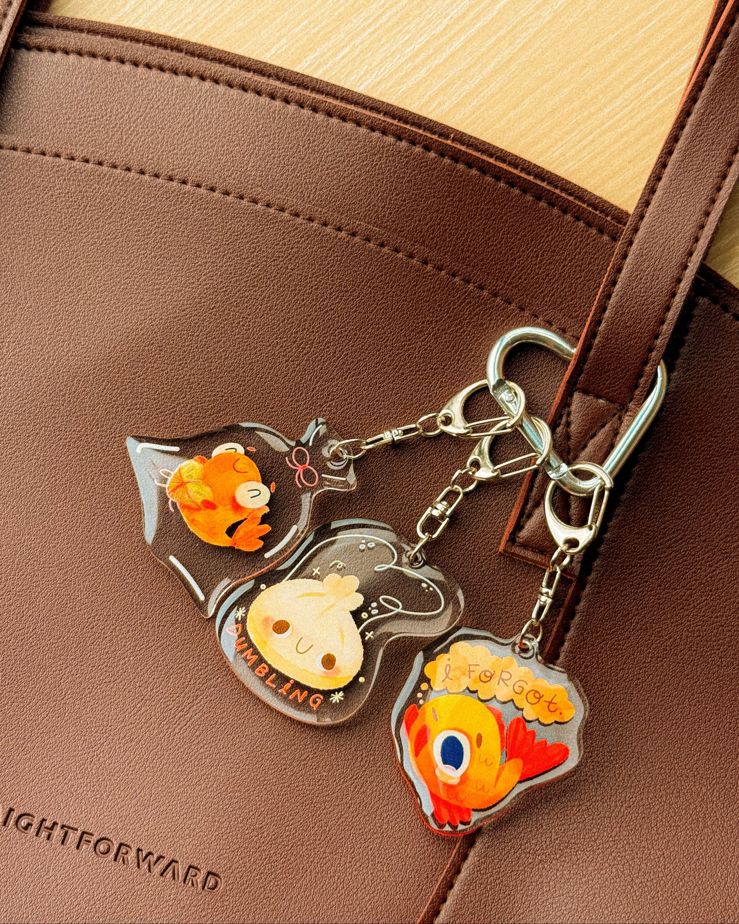 Three cartoon fish keychains on a brown leather bag.