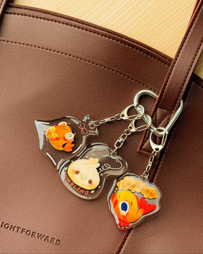 Three cartoon fish keychains on a brown leather bag.